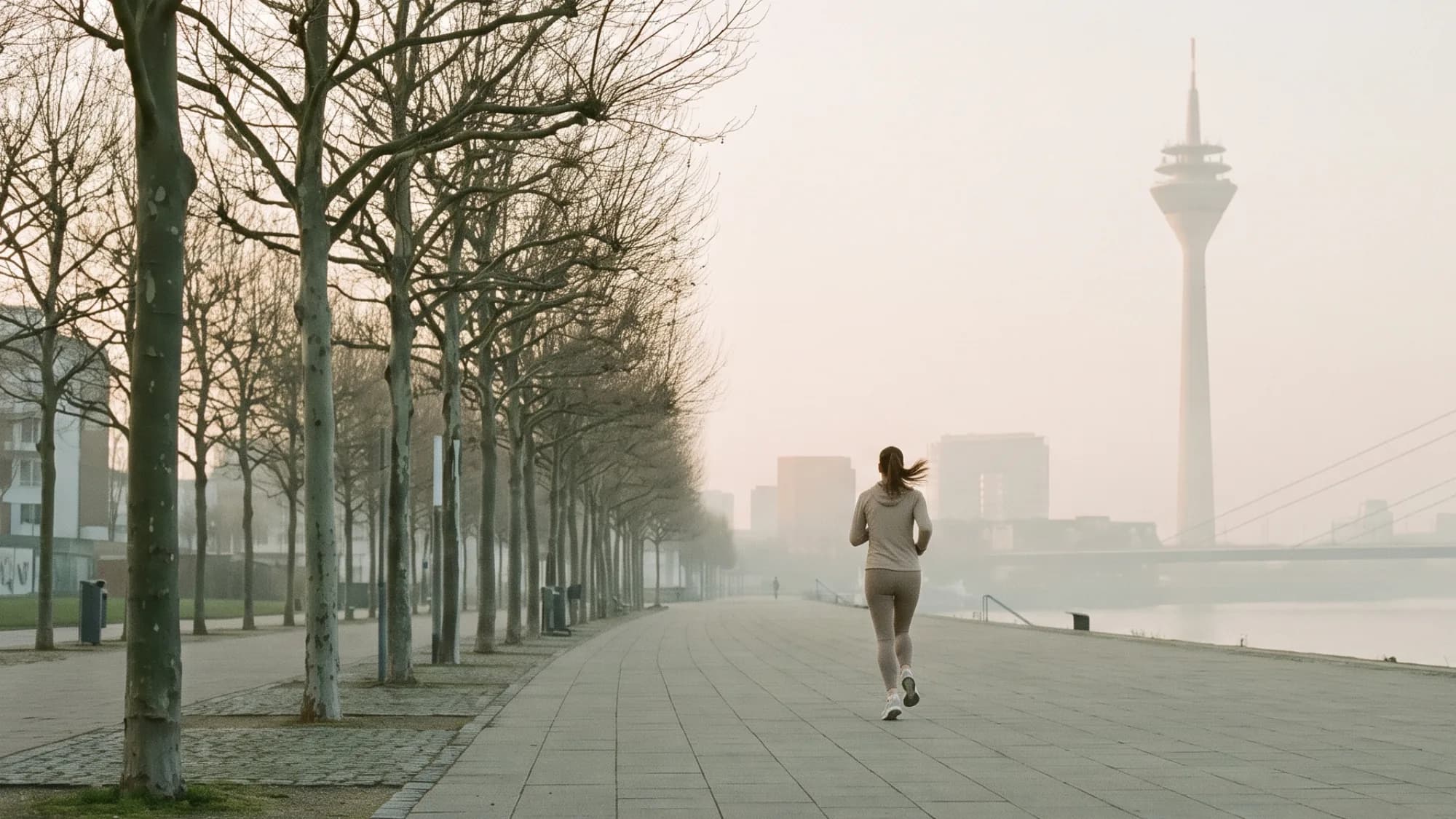 Läuferin auf der Rheinuferpromenade in Düsseldorf, rechts Rheinturm und Rheinkniebrücke im Morgendunst